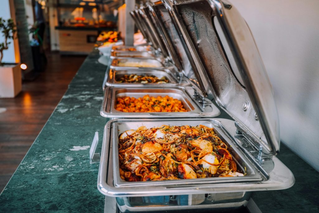 Buffet table with chafing dishes filled with various dishes and colorful food.