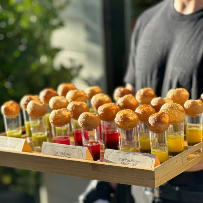 A tray of colorful drinks served in shot glasses with round tops.